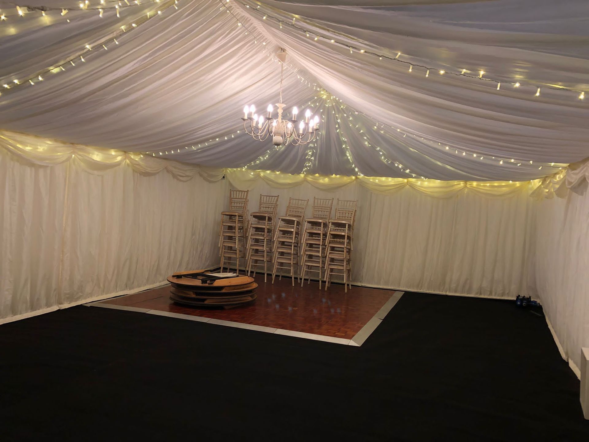 a room with a dance floor and chairs under a tent .