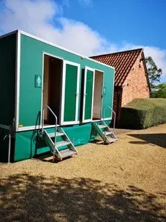 A green trailer with stairs leading up to it is parked in front of a brick building.