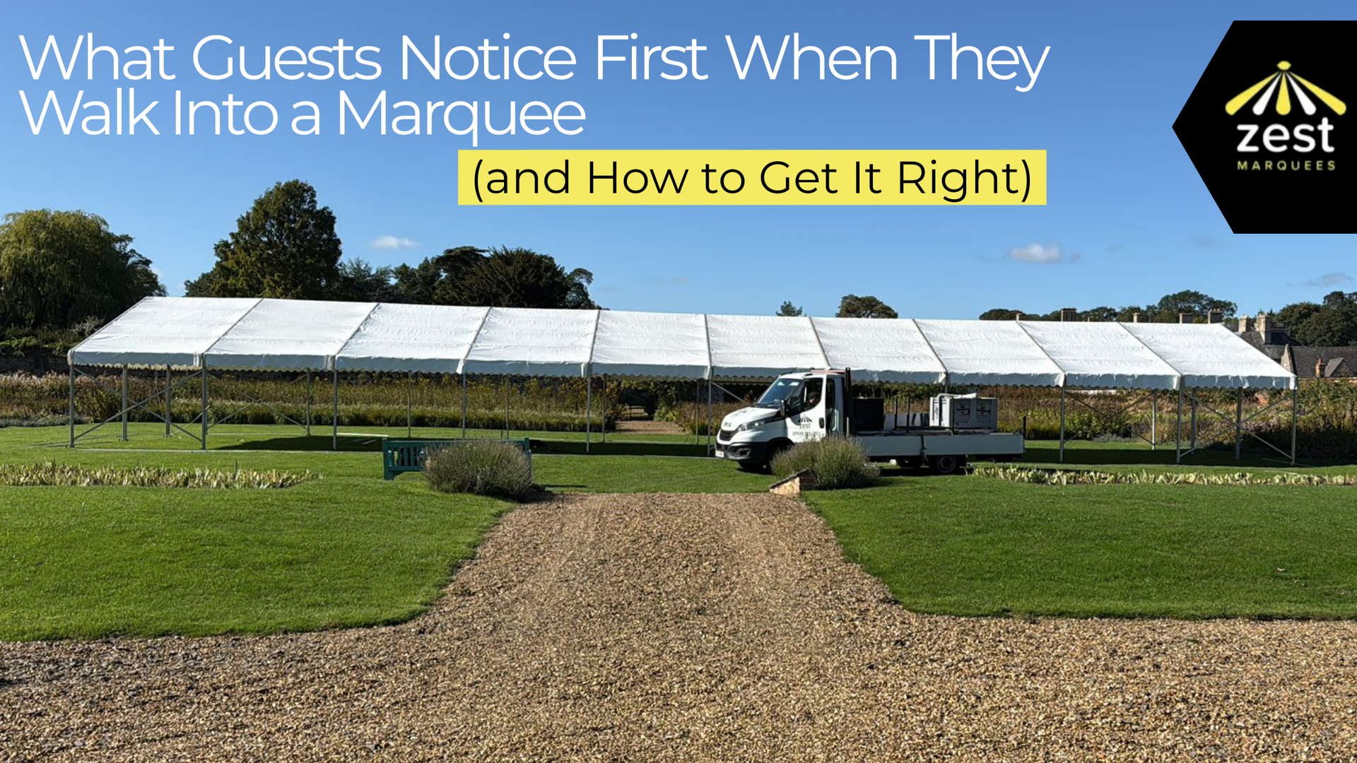 A white marquee set up on a grassy lawn with a gravel path leading to the entrance; trees in the background.