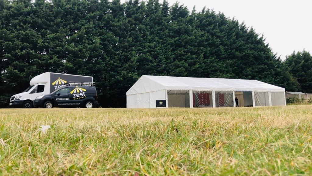A white van is parked in a grassy field next to a tent.