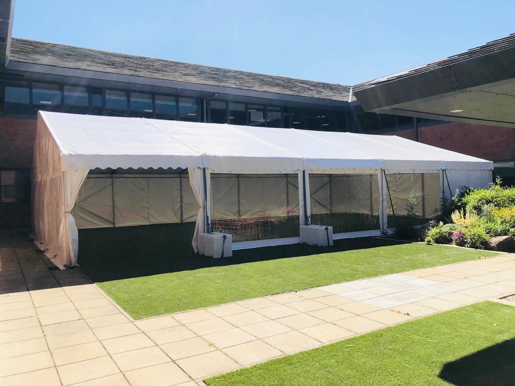 A large white tent is sitting in the grass in front of a building.