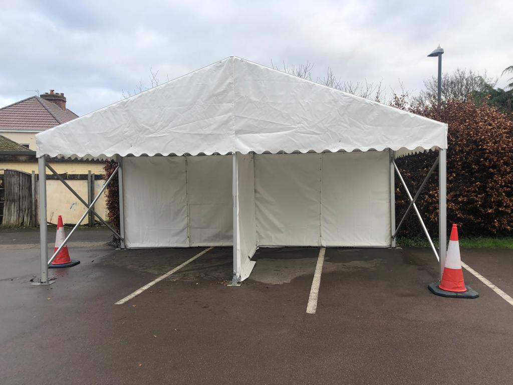 A white tent is sitting in a parking lot next to two orange and white traffic cones.