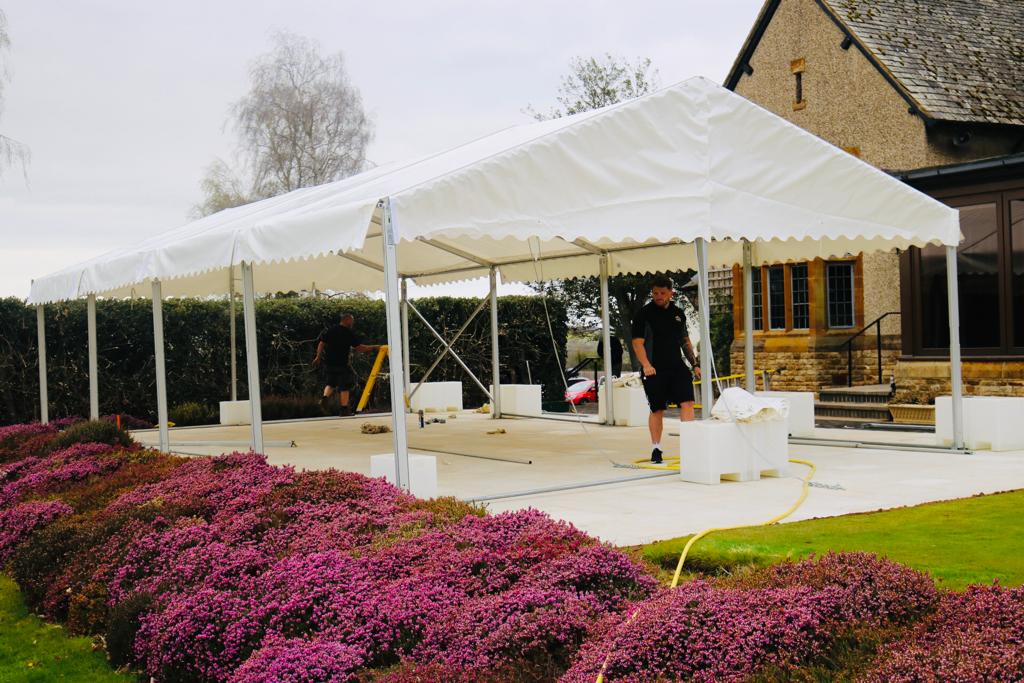 A man is standing under a white tent in front of a house.