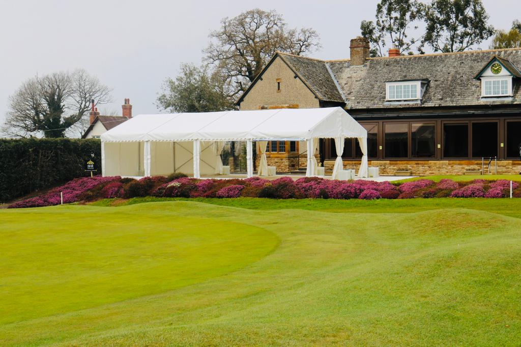 A large white tent is sitting on top of a lush green field in front of a house.