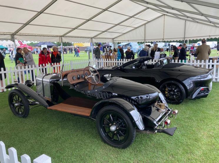 Two cars are parked under a tent in a field.