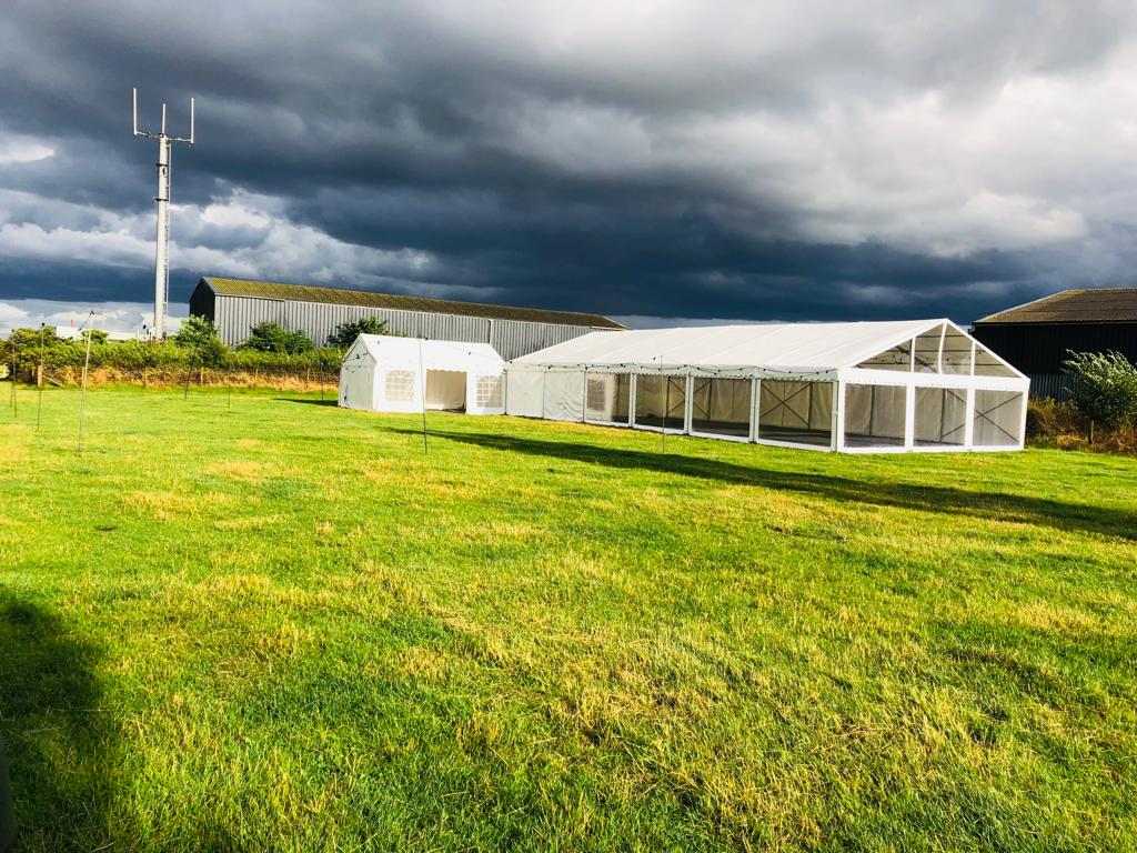 A row of tents are sitting in a grassy field under a cloudy sky.