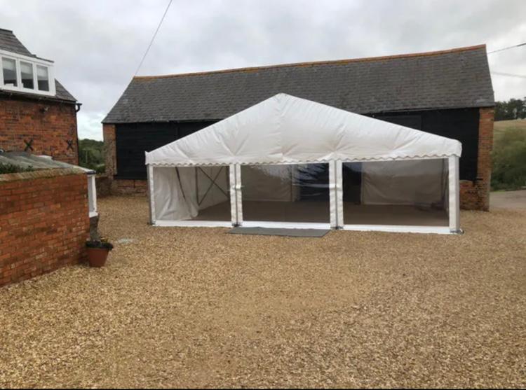 A large white tent is sitting in front of a barn.
