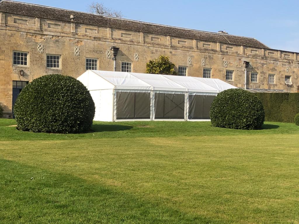 A large white tent is sitting in the grass in front of a building.