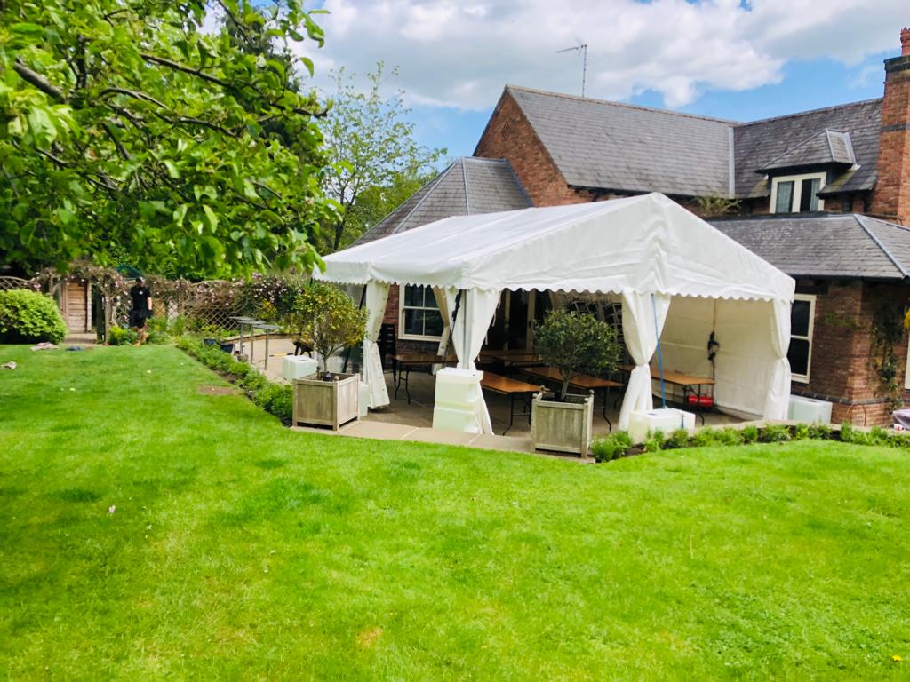 A large white tent is sitting in the grass in front of a house.