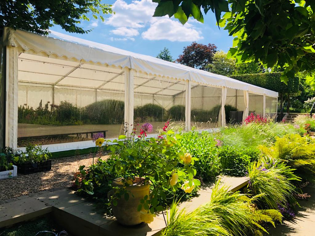 A white tent is sitting in the middle of a garden surrounded by potted plants.