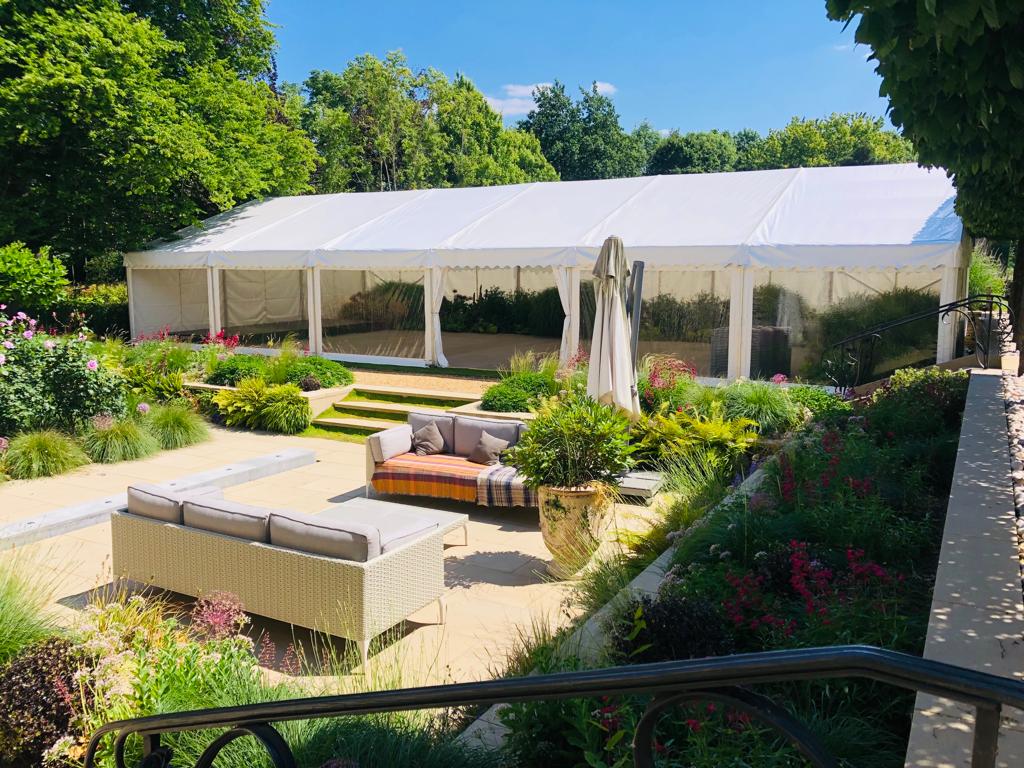A large white tent is sitting in the middle of a garden.