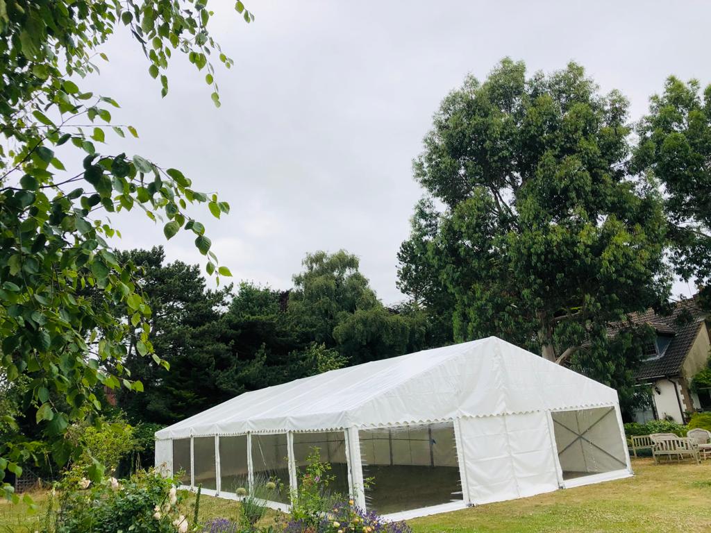 A large white tent is sitting in the middle of a field surrounded by trees.