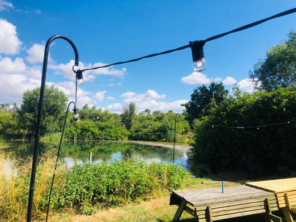 A picnic table in front of a lake with a string of lights hanging from a pole.