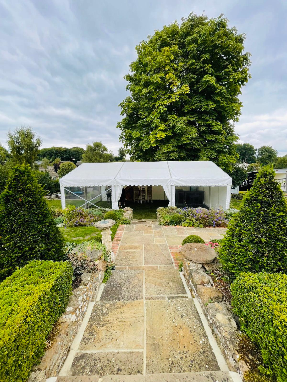 A large white tent is sitting in the middle of a garden.