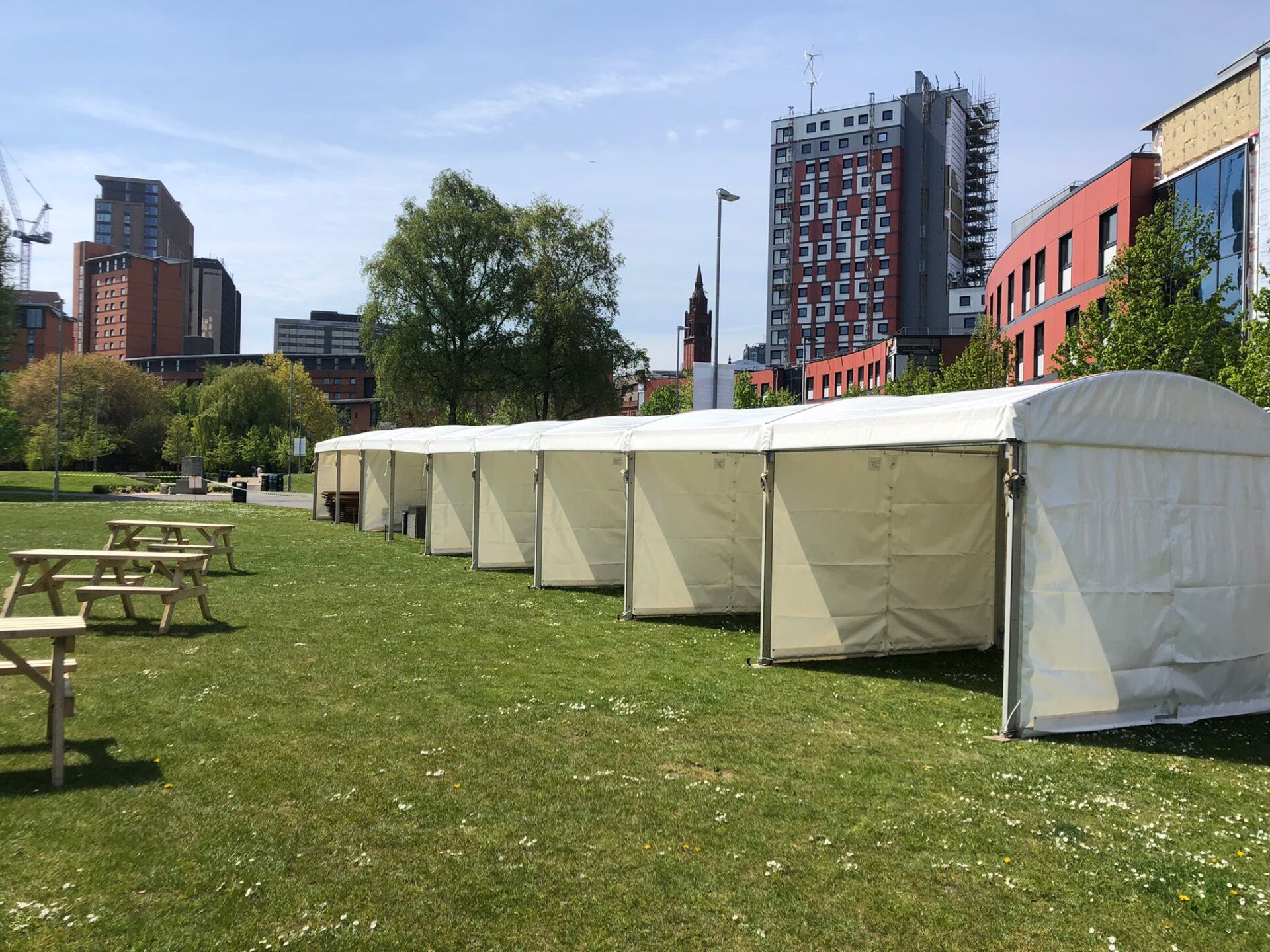 A row of white tents and picnic tables in a park.