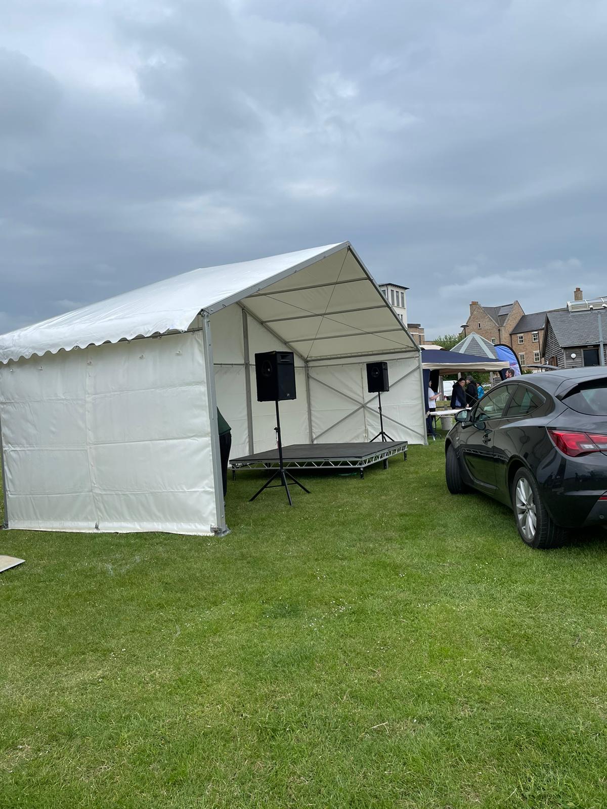 A car is parked in front of a white tent in a grassy field.