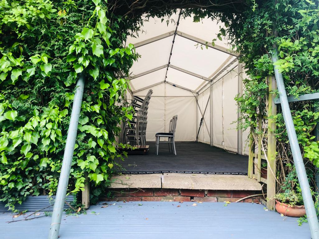 A white tent with chairs inside of it is surrounded by ivy.