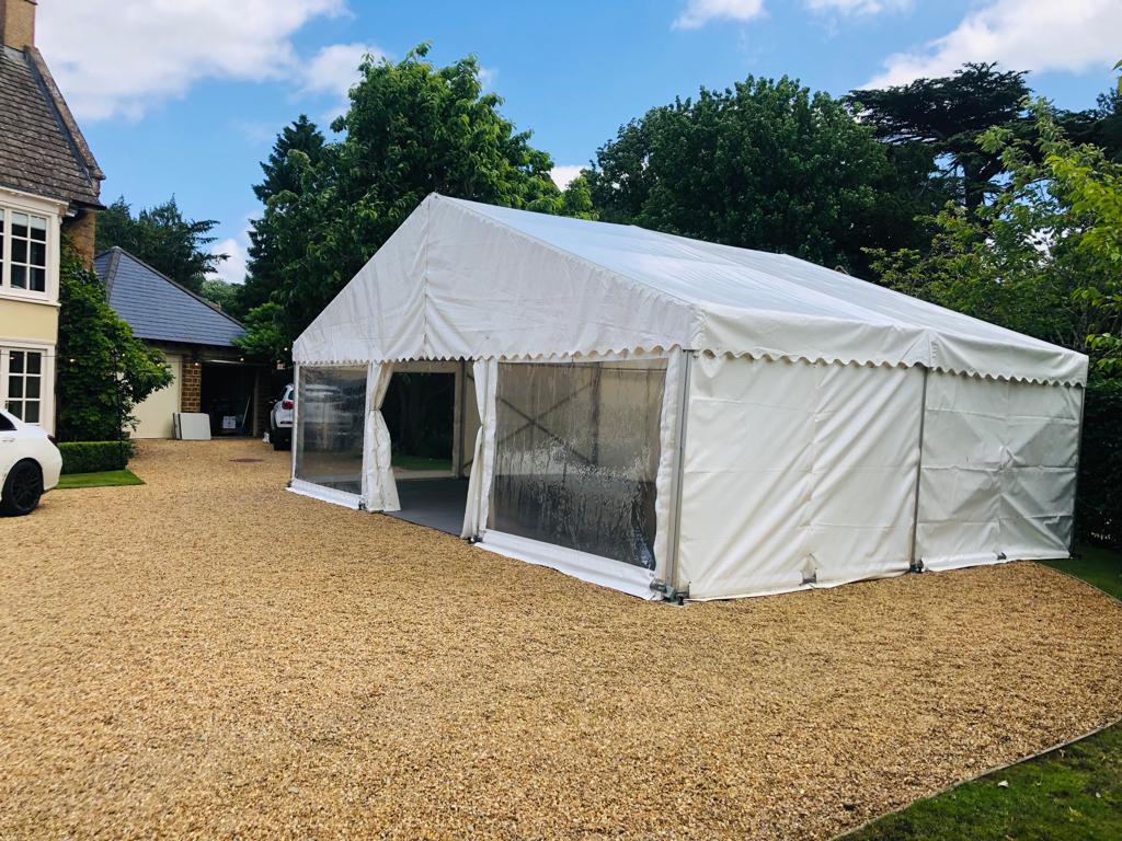 A large white tent is sitting in a gravel driveway in front of a house.