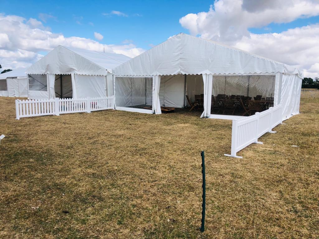 A large white tent is sitting in the middle of a field next to a white fence.