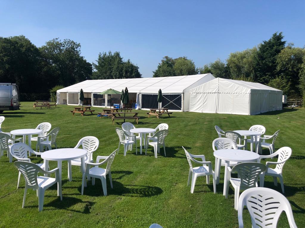 There are many tables and chairs in the grass in front of a tent.