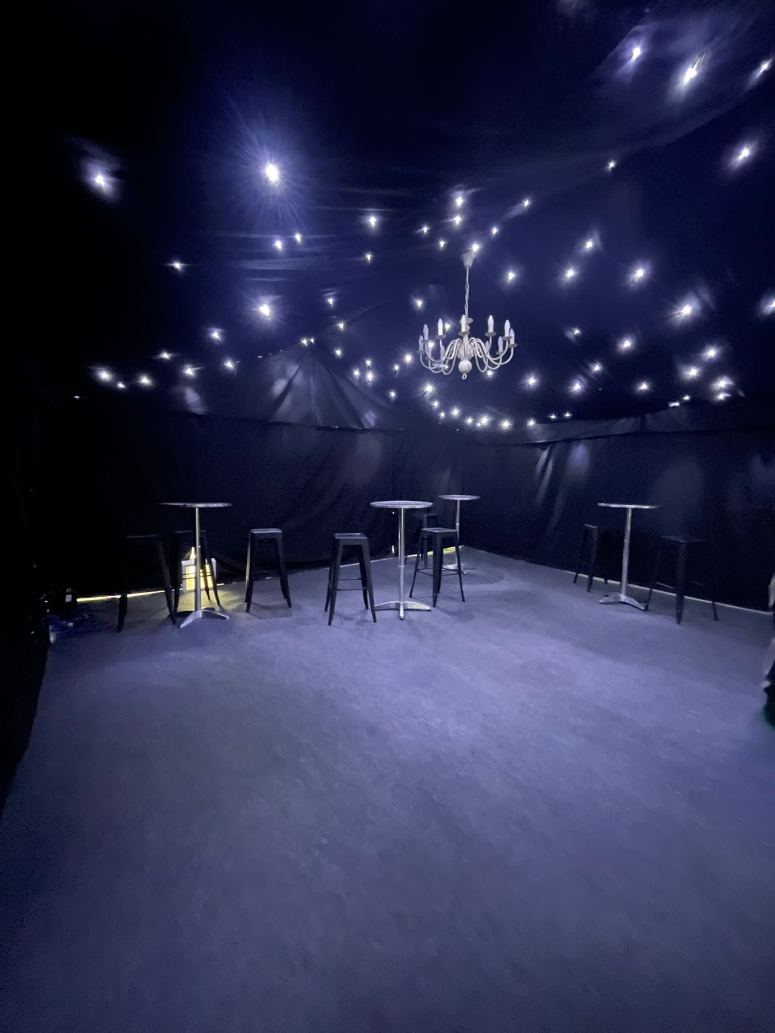 A dark room with tables and chairs and a chandelier hanging from the ceiling