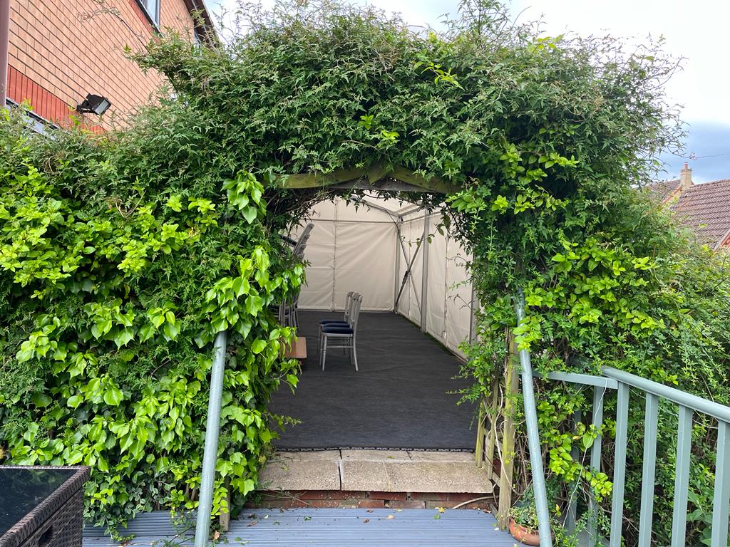 A white tent is surrounded by a lush green hedge.