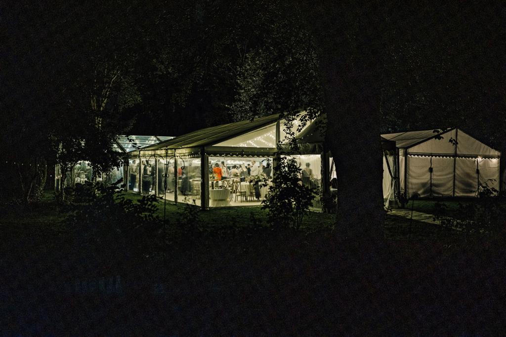 A large tent is lit up at night in the woods.