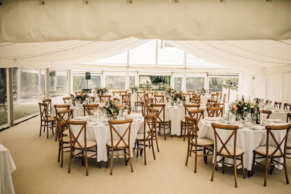 A large tent with tables and chairs set up for a wedding reception.