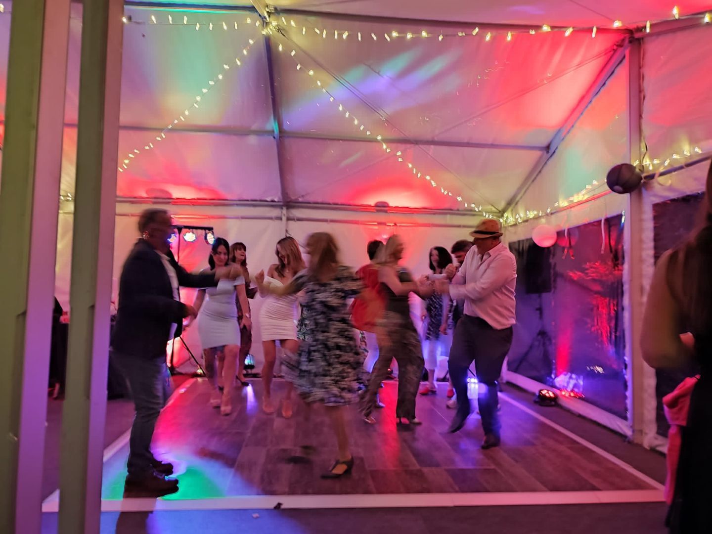 A group of people are dancing in a tent at a party.