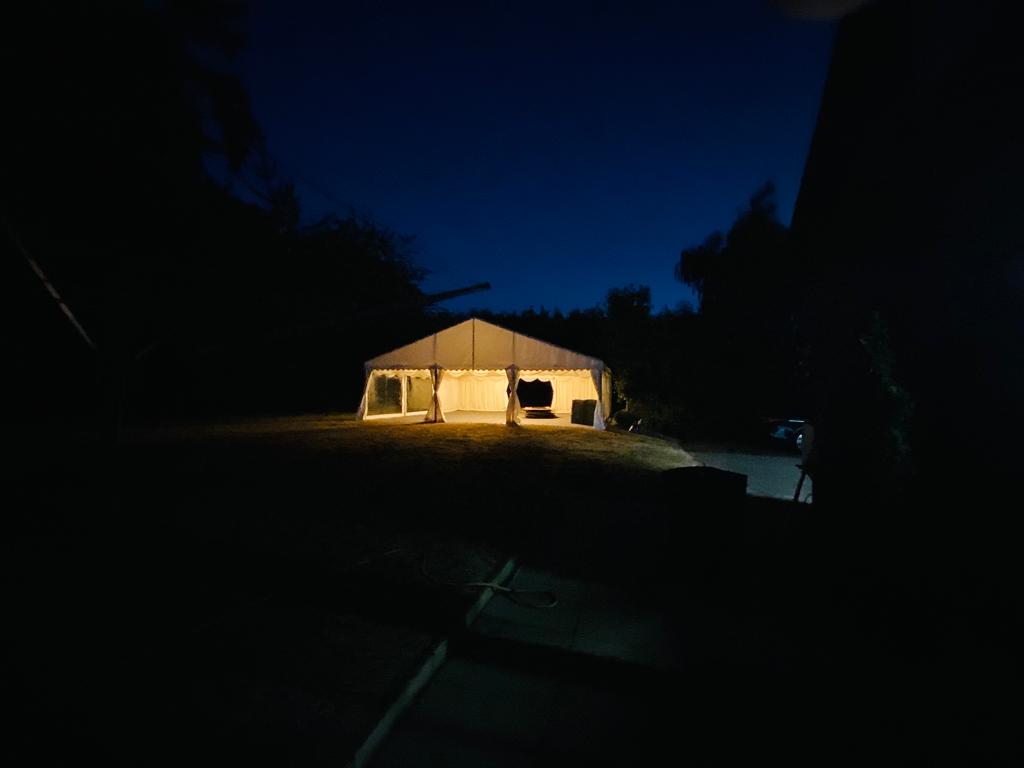 A tent is lit up at night in a dark parking lot.