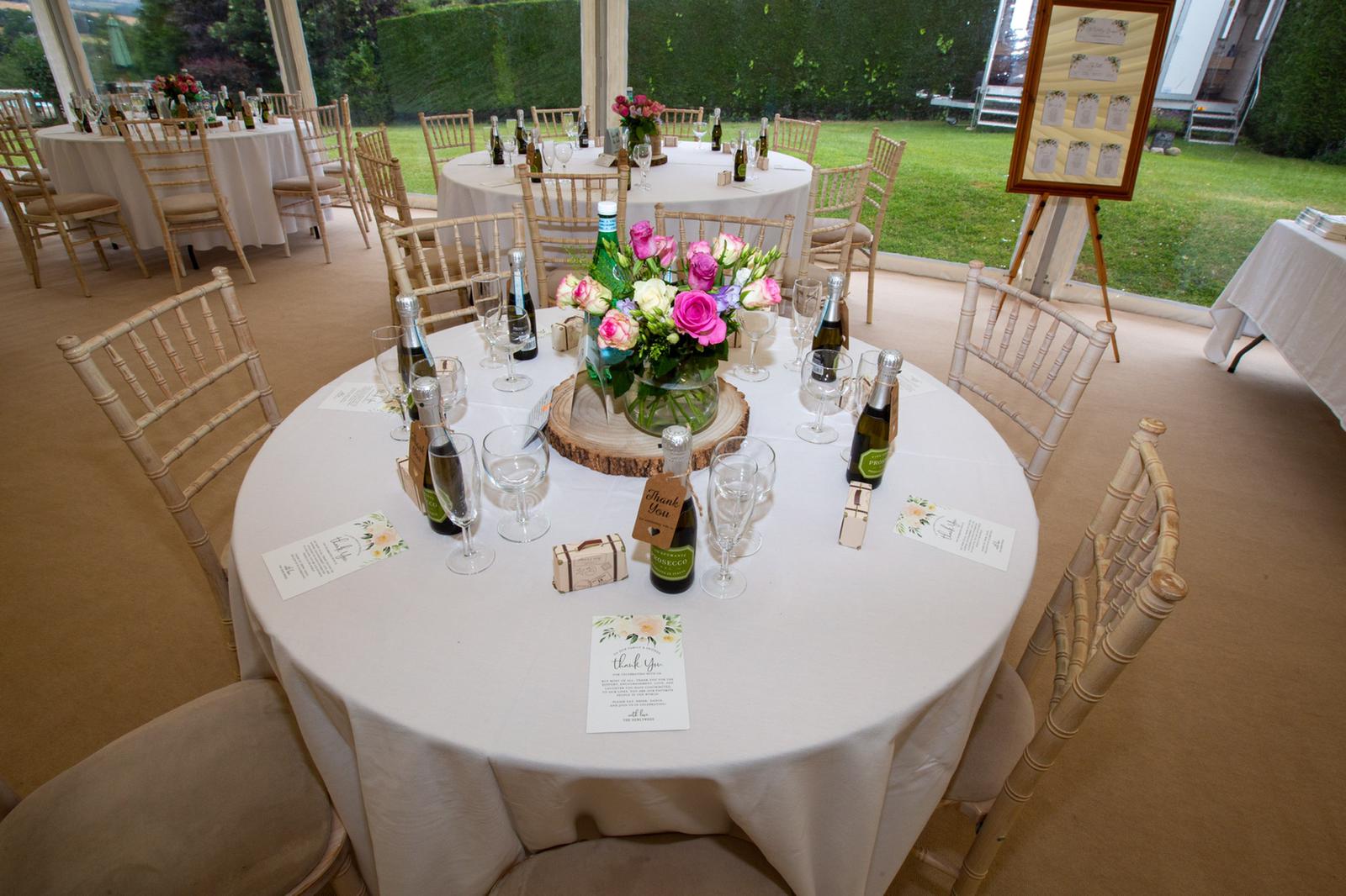 A table with a vase of flowers on it is set for a wedding reception.