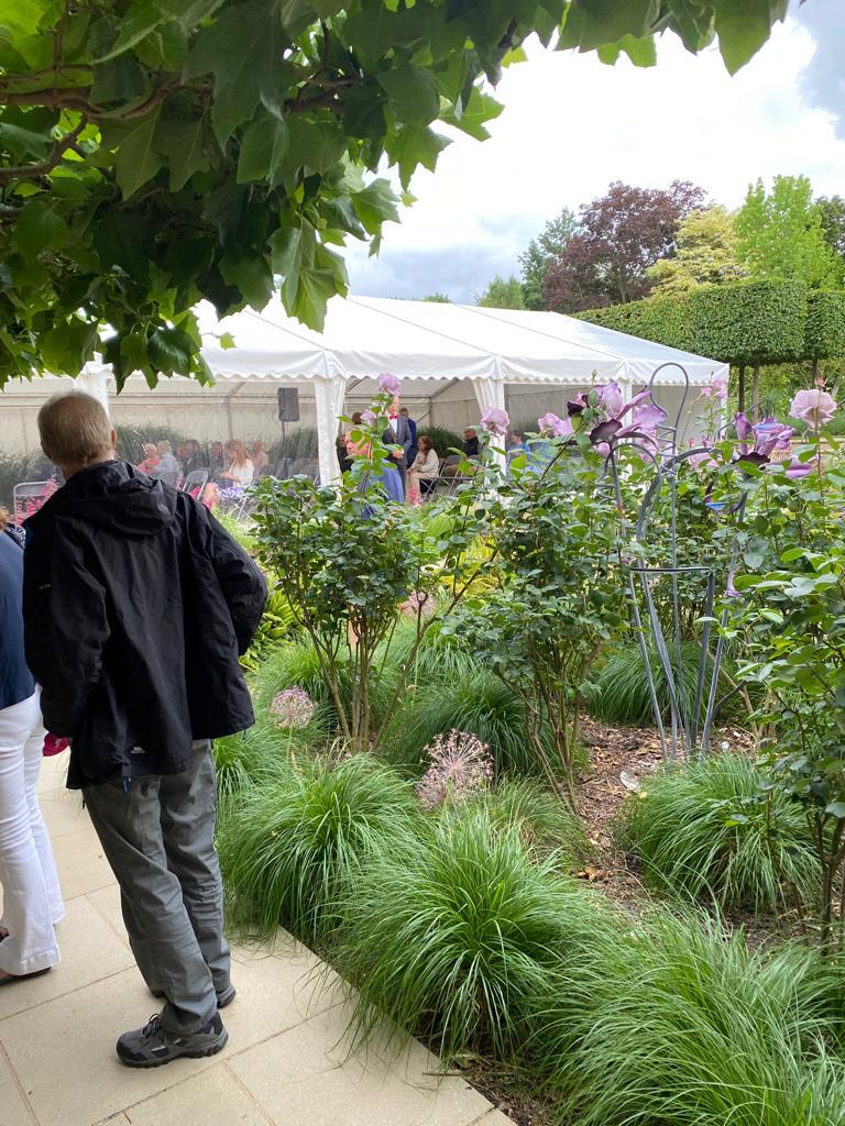 A man is standing in a garden in front of a white tent.