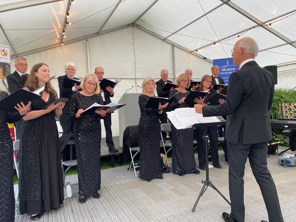 A choir is singing in front of a man in a suit.