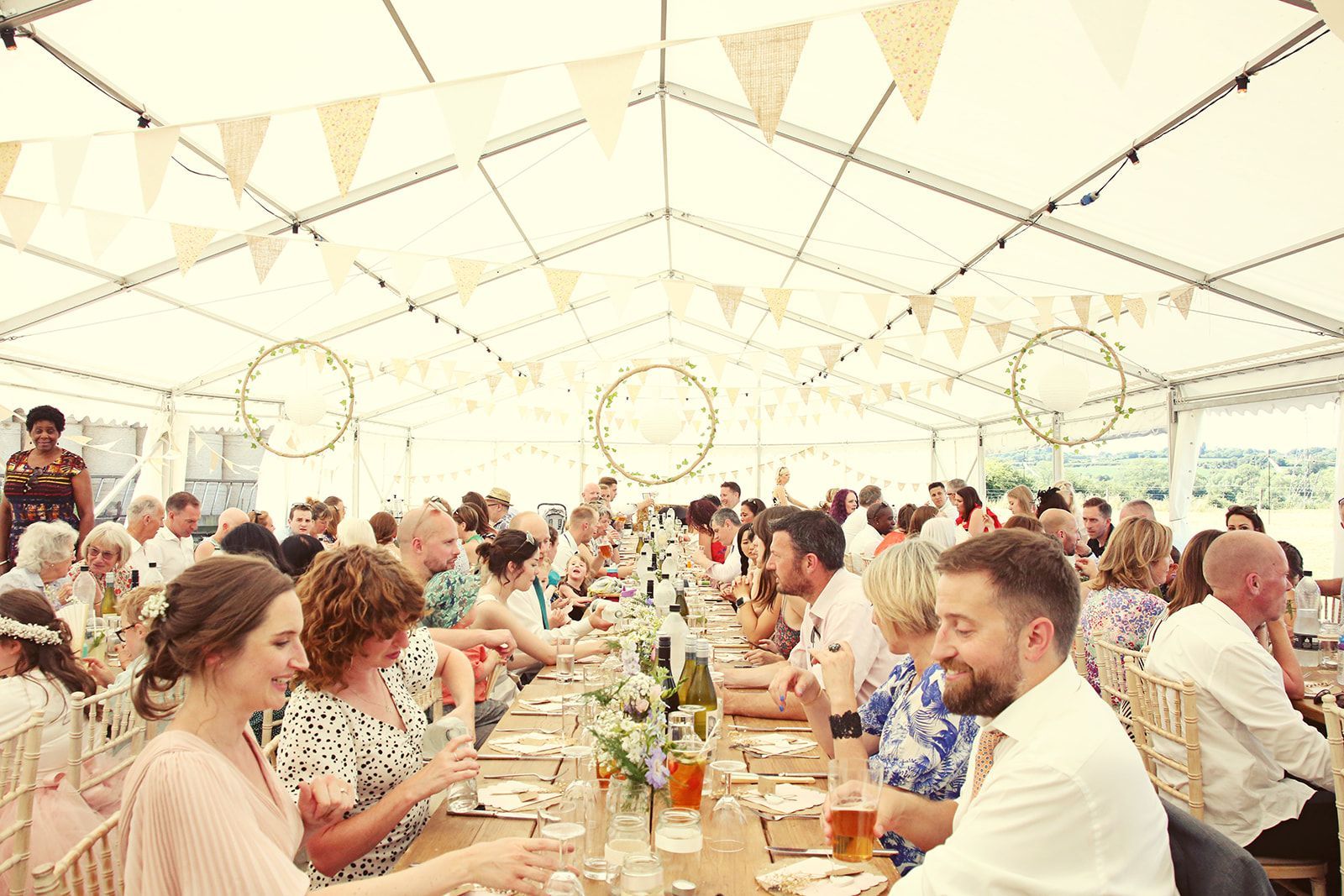 A large group of people are sitting at a long table in a tent.