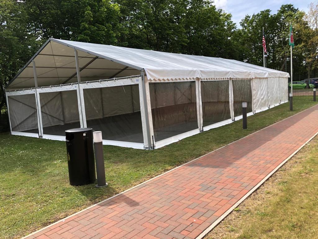A large white tent is sitting on top of a lush green field next to a brick walkway.