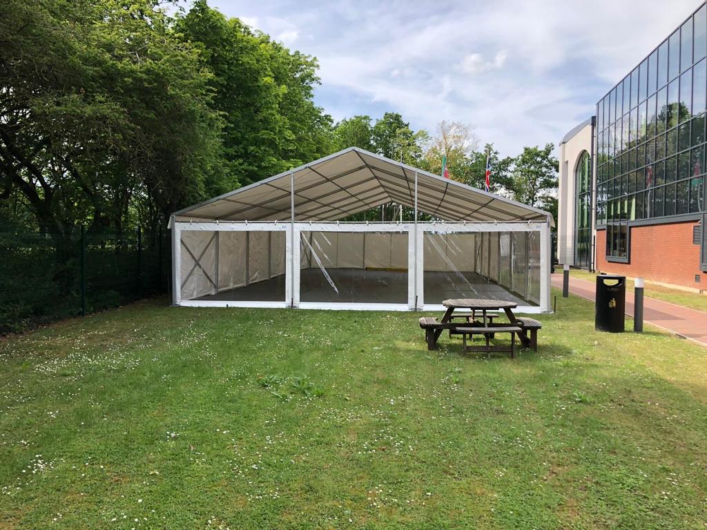 A large white tent is sitting in the middle of a grassy field next to a picnic table.