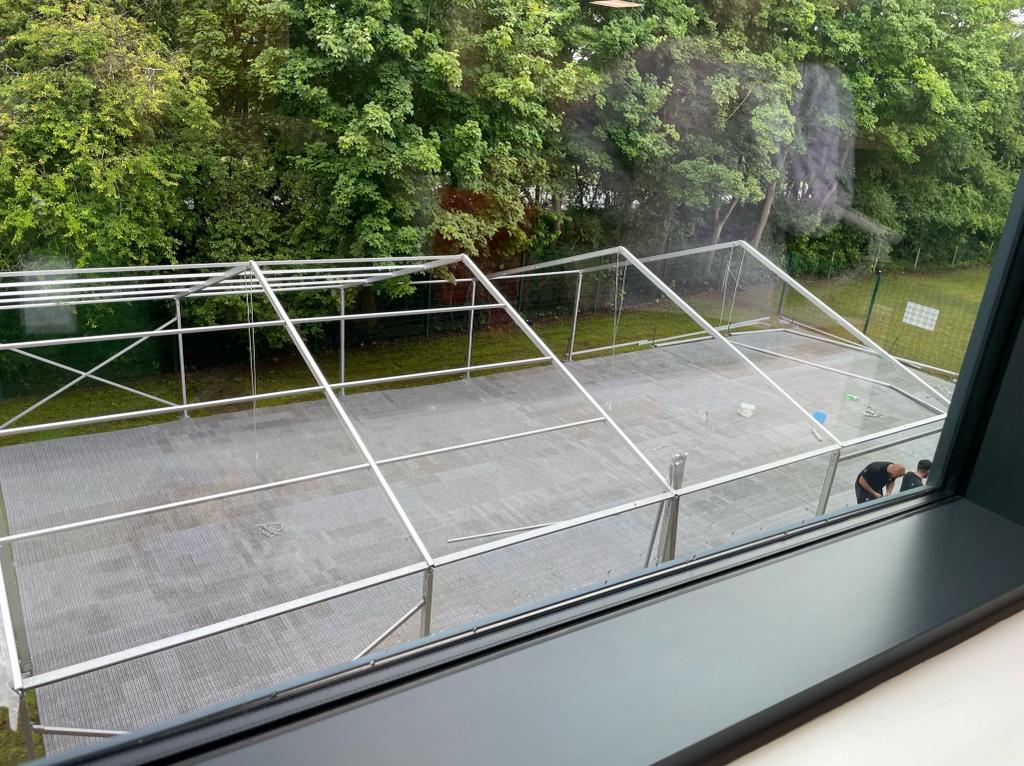 A view of a clear tent from a window with trees in the background