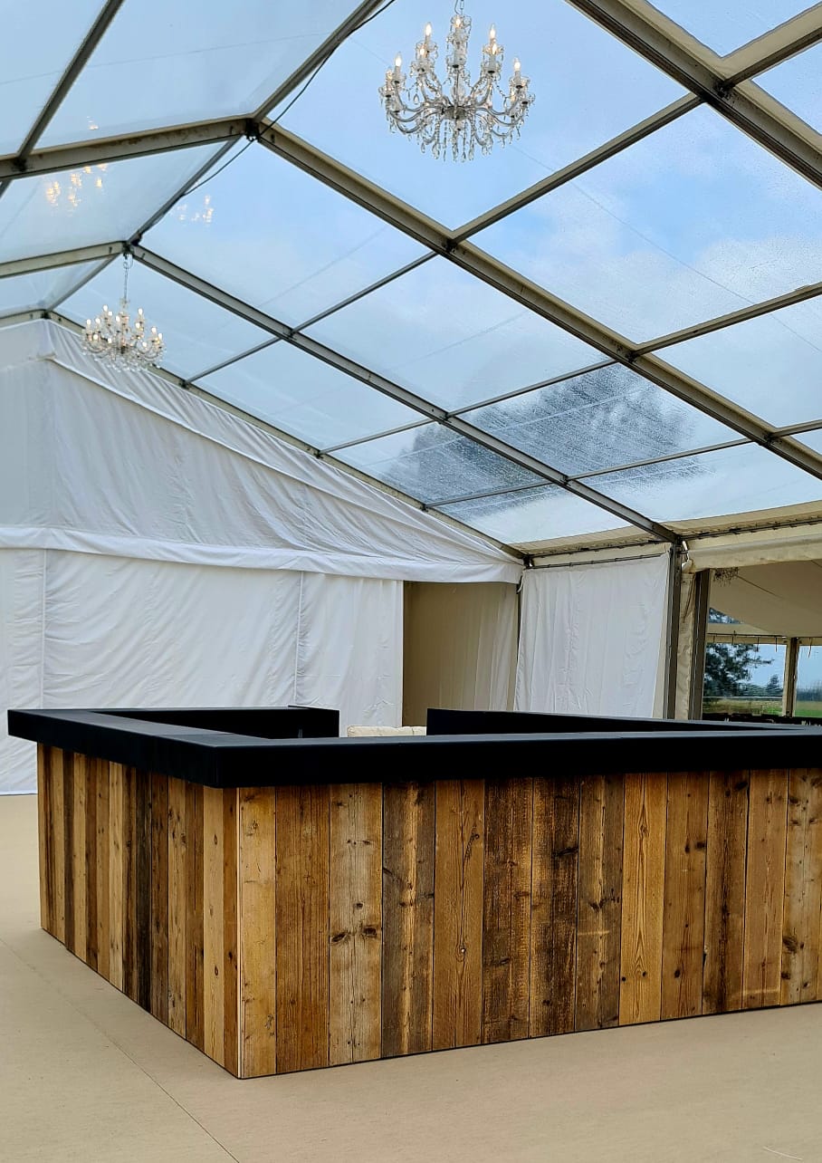 A wooden bar under a clear roof with a chandelier hanging from the ceiling