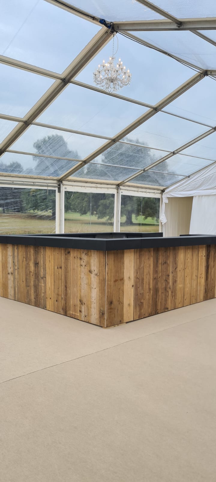 A wooden bar in a clear tent with a chandelier hanging from the ceiling.