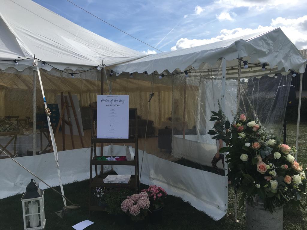 A white tent with a sign on it and flowers in front of it.