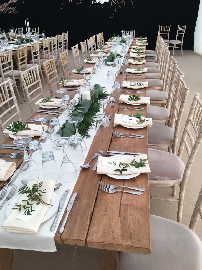 A long wooden table with plates , glasses , and silverware on it.