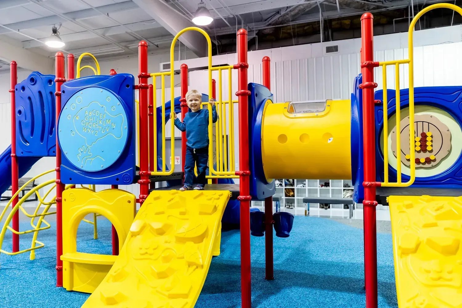 Child on a colorful indoor playground with climbing wall, tunnel, and slides.