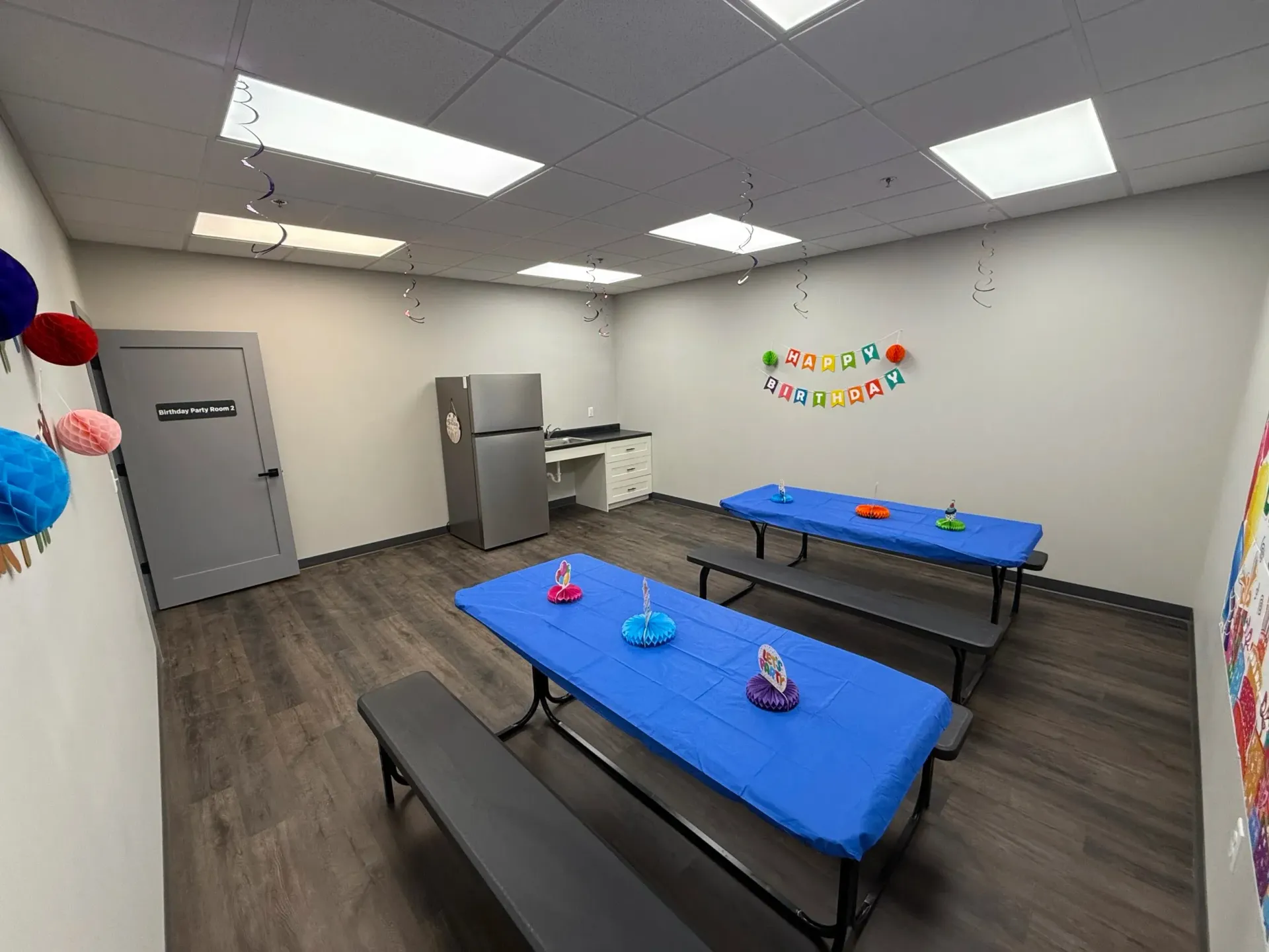 Party room with blue-covered tables, black benches, refrigerator, and decorations.