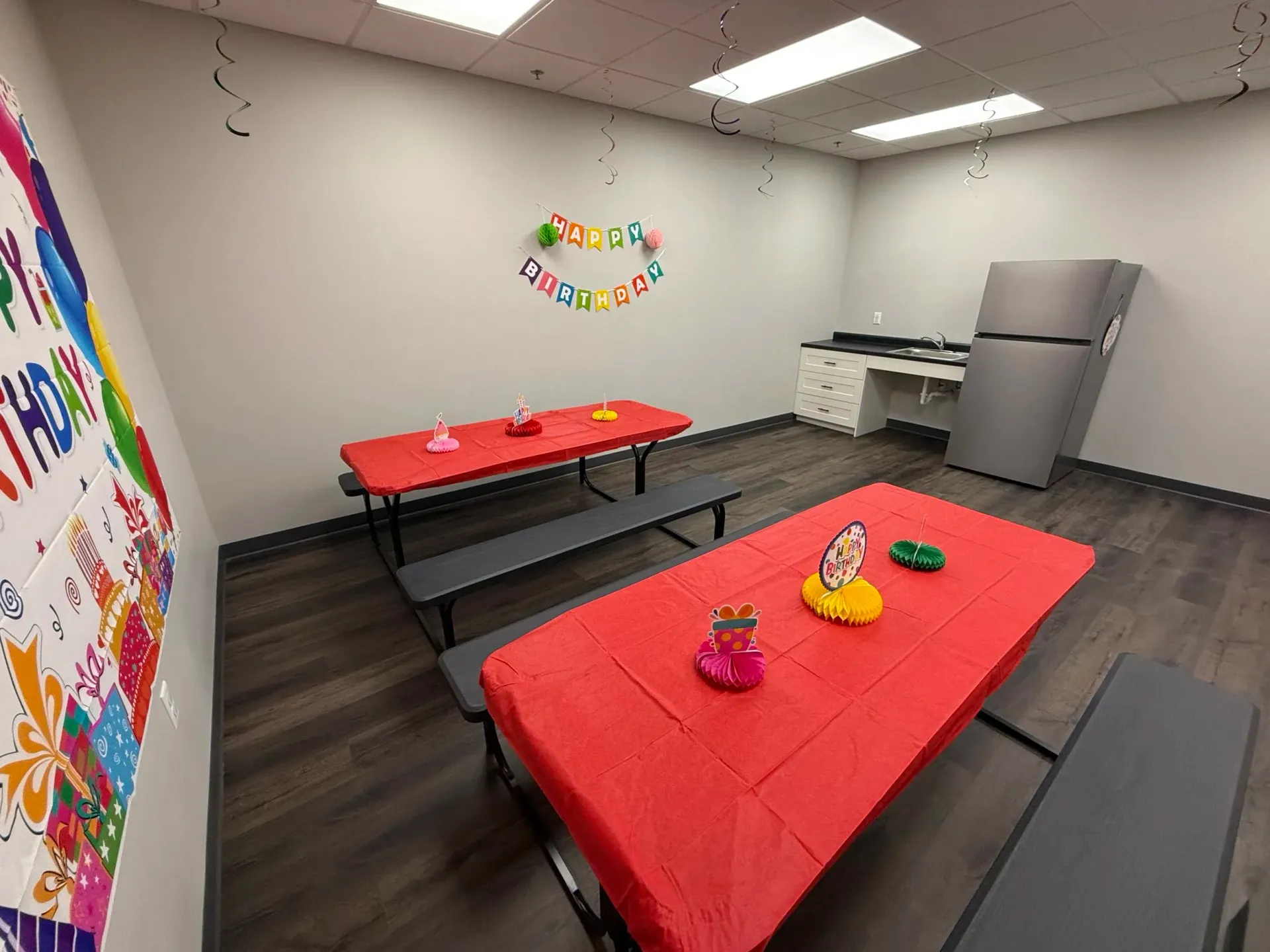 Party room with red-covered tables, picnic benches, and birthday decorations.