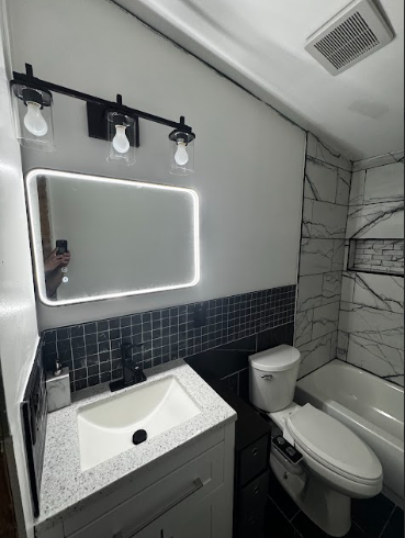 A modern bathroom with a white sink, terrazzo-style vanity top, black backsplash, LED mirror, and black vanity lighting.