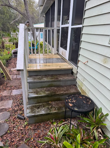 A set of weathered wooden steps leading up to a house’s screened-in porch, with a newly built landing platform at the top.