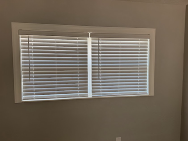 A rectangular window with closed white horizontal blinds set into a neutral-colored wall.