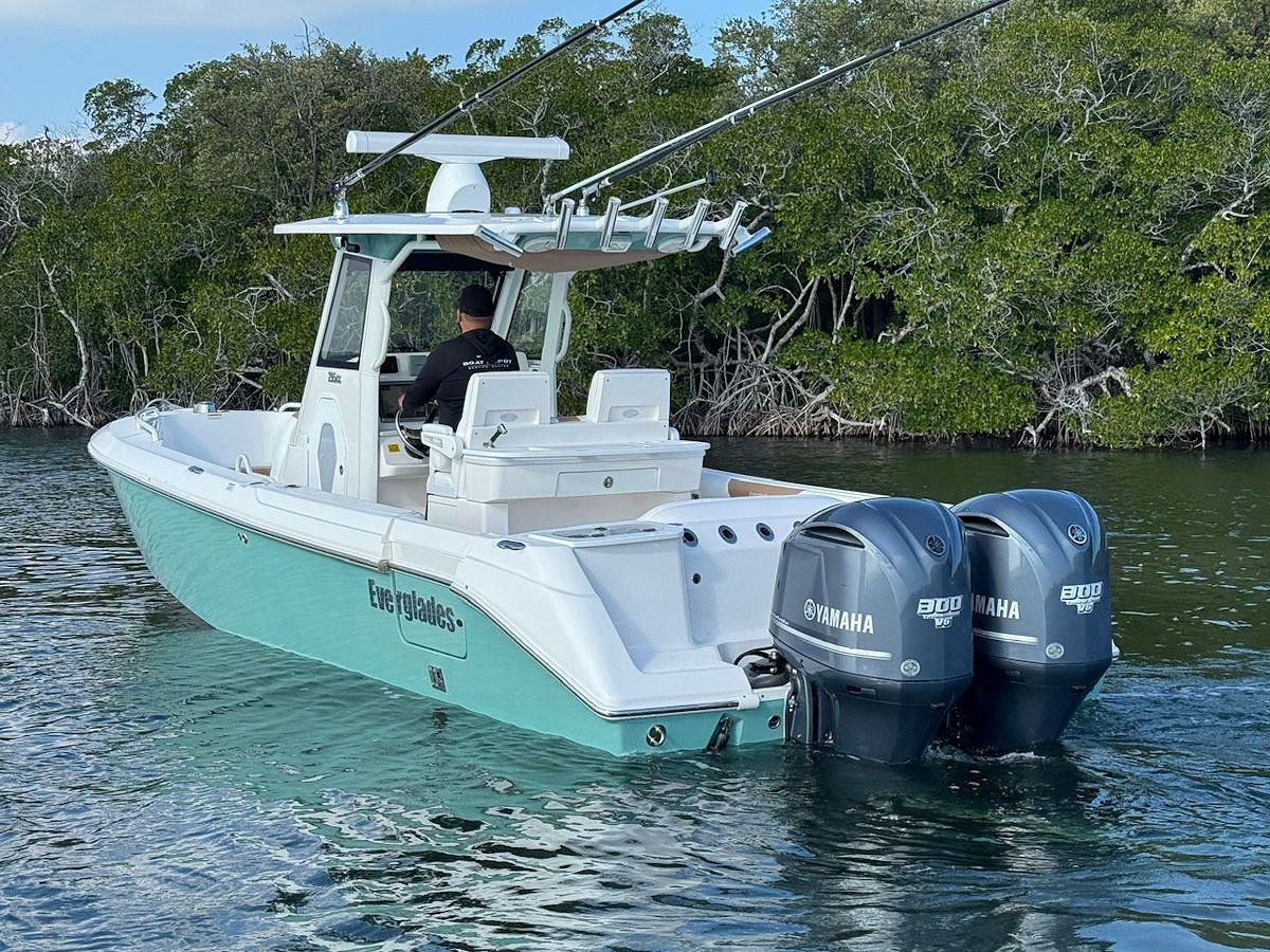Boat with turquoise hull and two outboard motors on water, pilot at helm.