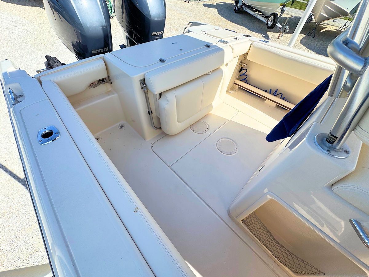 Boat deck interior with cream-colored surfaces, including seating, storage, and fishing rod holders. Dual outboard motors visible.