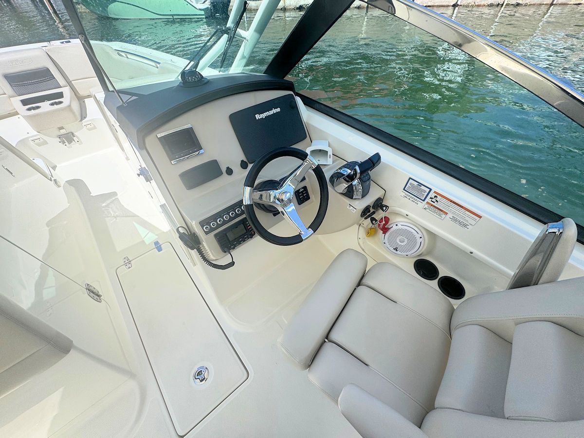 Boat cockpit with steering wheel, gauges, seats, and windshield, on a sunny day.